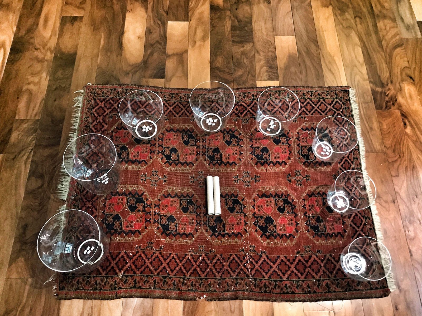 Eight clear quartz singing bowls arranged on an antique red rug and photographed from directly above, a small round maker's sticker visible inside each one