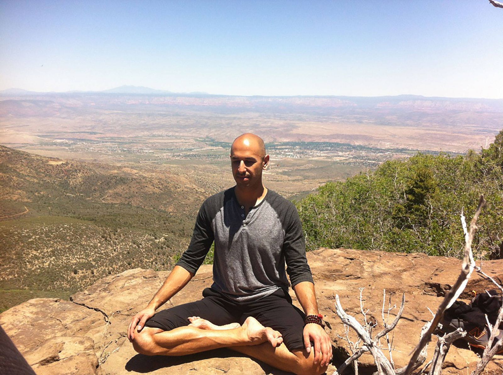 Hamid sitting cross legged on a rock ledge with his eyes closed, a wide Arizona valley opening out below him