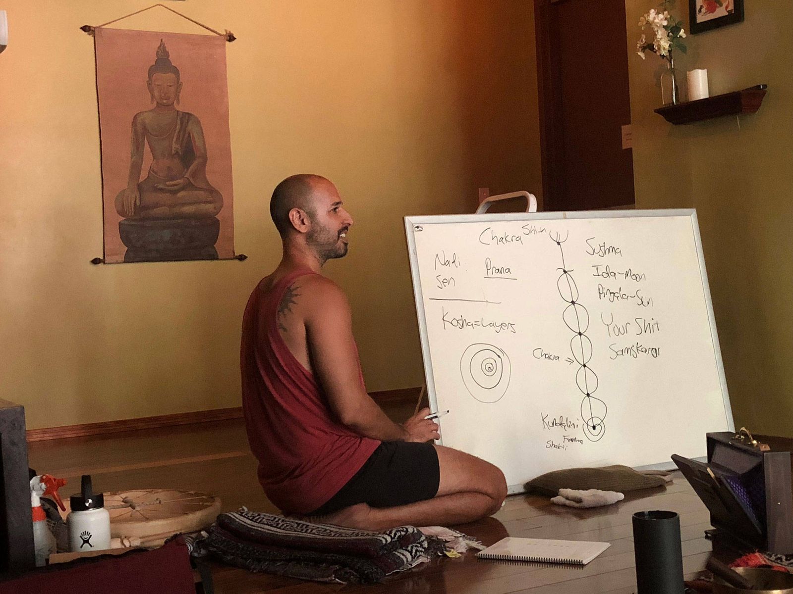Hamid sitting cross legged on the floor teaching from a handwritten whiteboard, a hanging scroll behind him