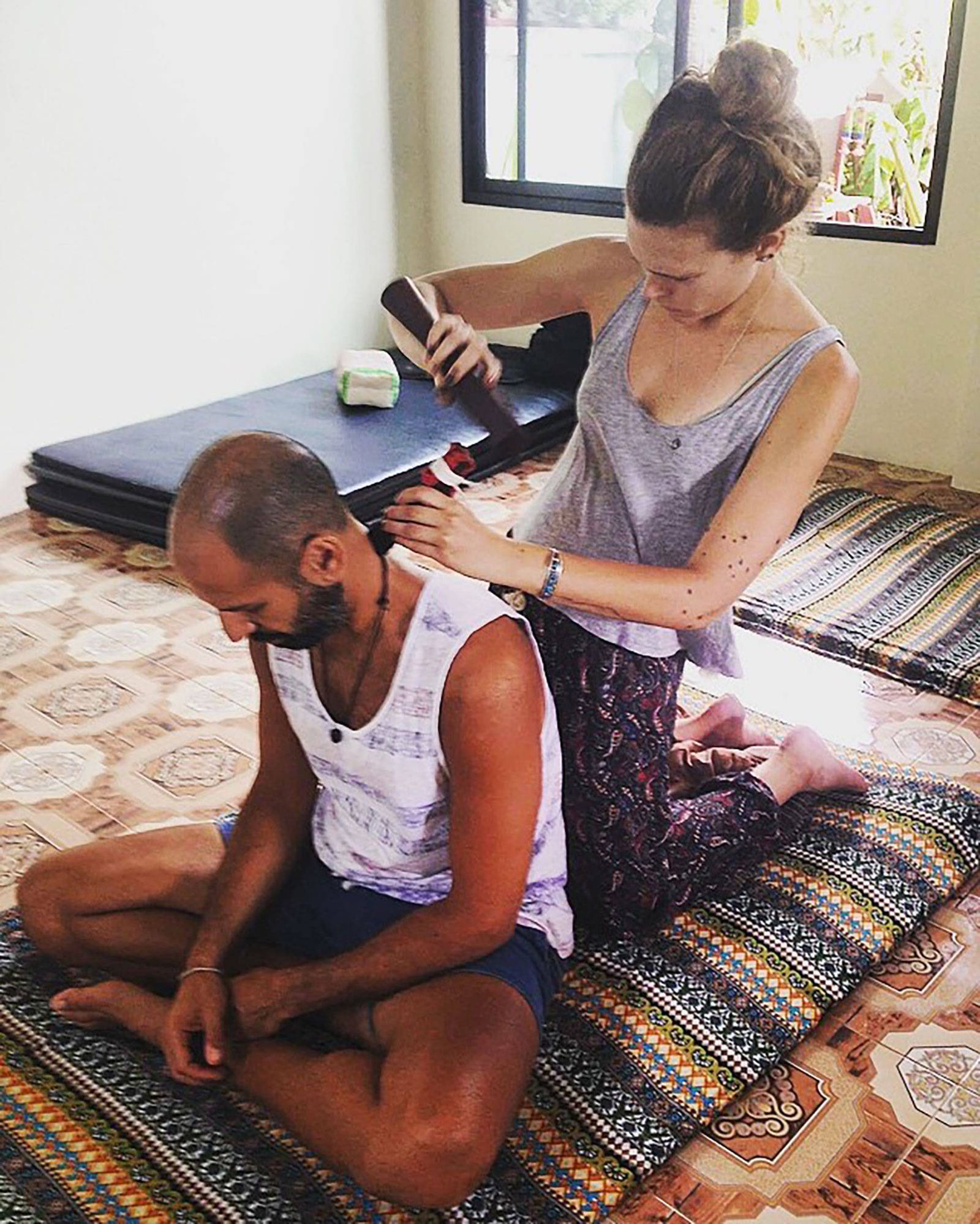 A student practising Tok Sen on Hamid's shoulders as he sits cross legged on a Thai mat
